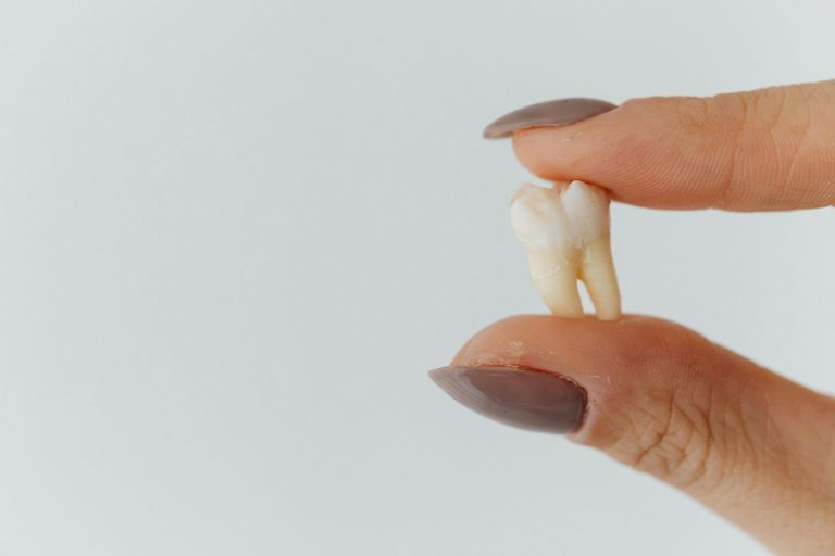hand with painted fingernails holds a tooth