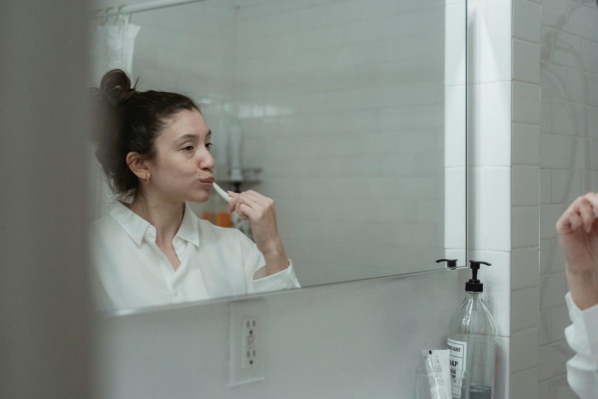 woman brushing her teeth in front of a bathroom mirror